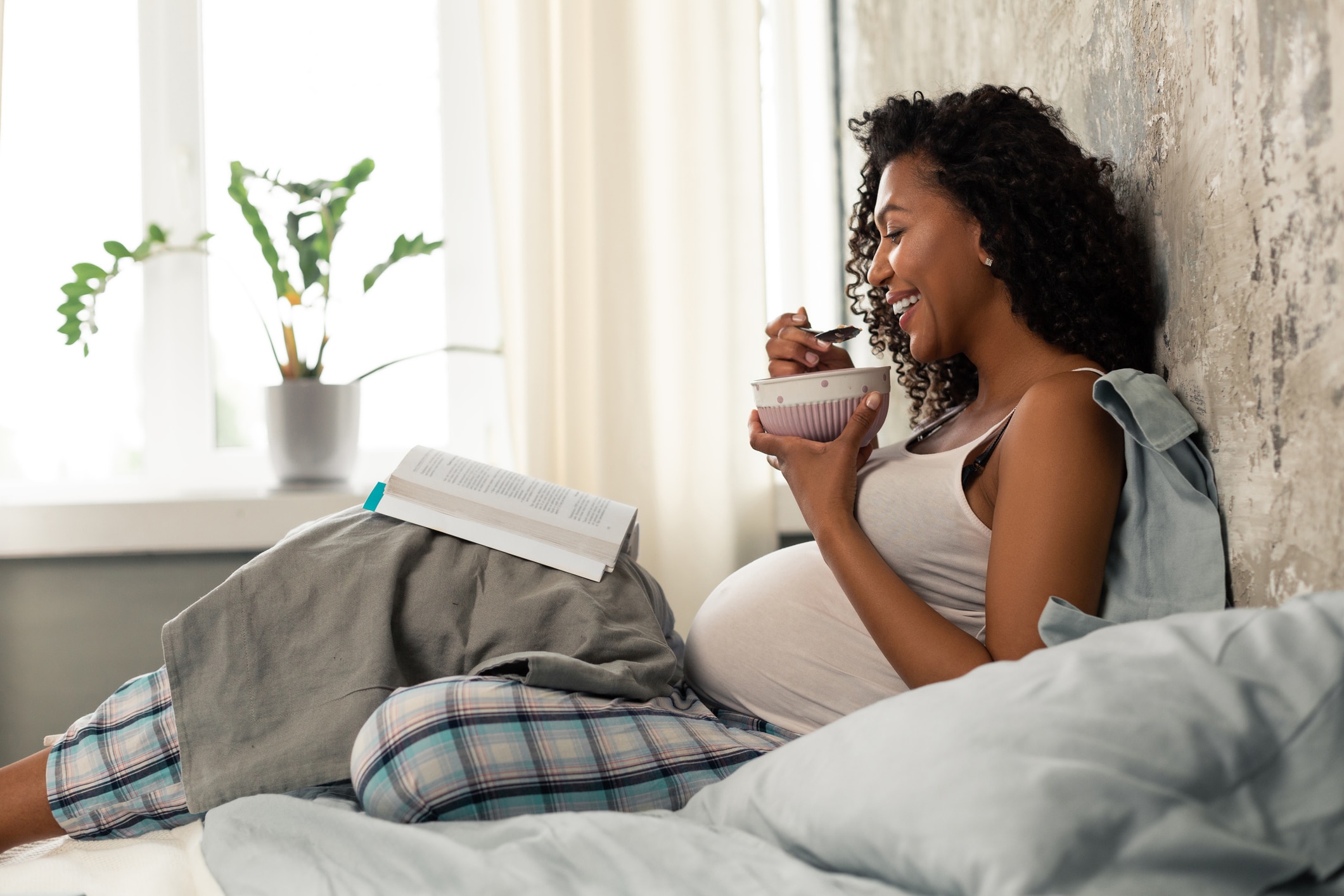 hyperemesis gravidarum - lachende zwangere vrouw eet yoghurt op de bank