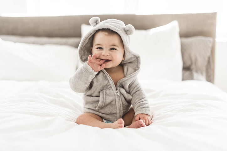 baby in schattig pakje zit op bed - beweging stimuleren bij een baby
