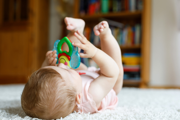 baby ligt op rug en speelt met speeltje - beweging stimuleren bij een baby