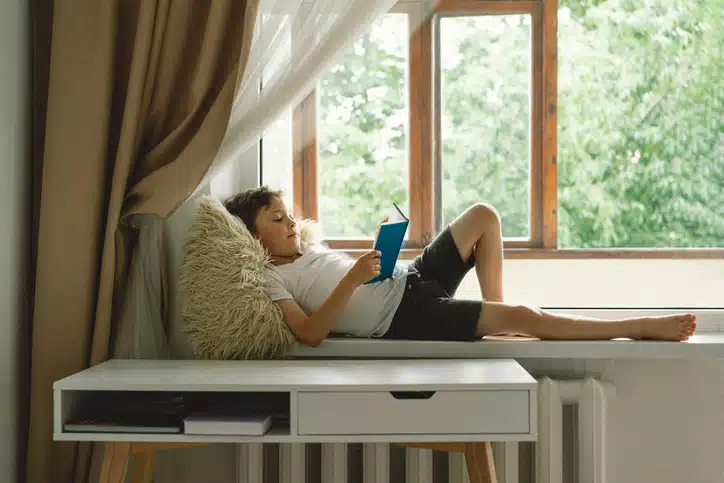 kind alleen thuis laten - jongen leest boek voor het raam