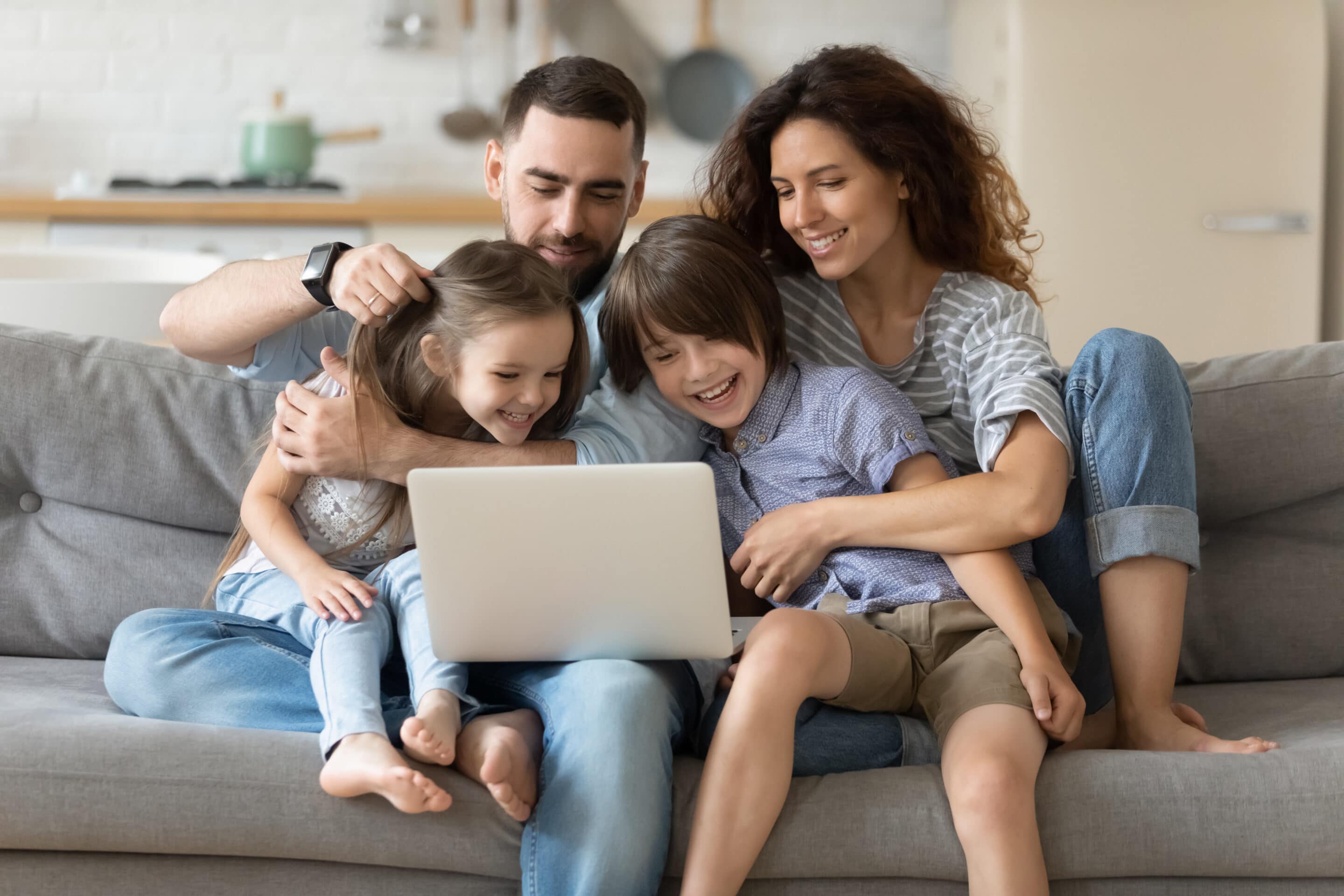 lachend gezin op de bank met laptop - zo houd je een goede relatie na kinderen