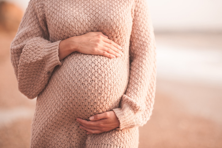zwangerschapsshoot - zwangere vrouw op het strand, handen om haar buik