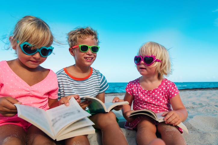 drie kinderen lezen op het strand - oefenen met lezen in de zomervakantie